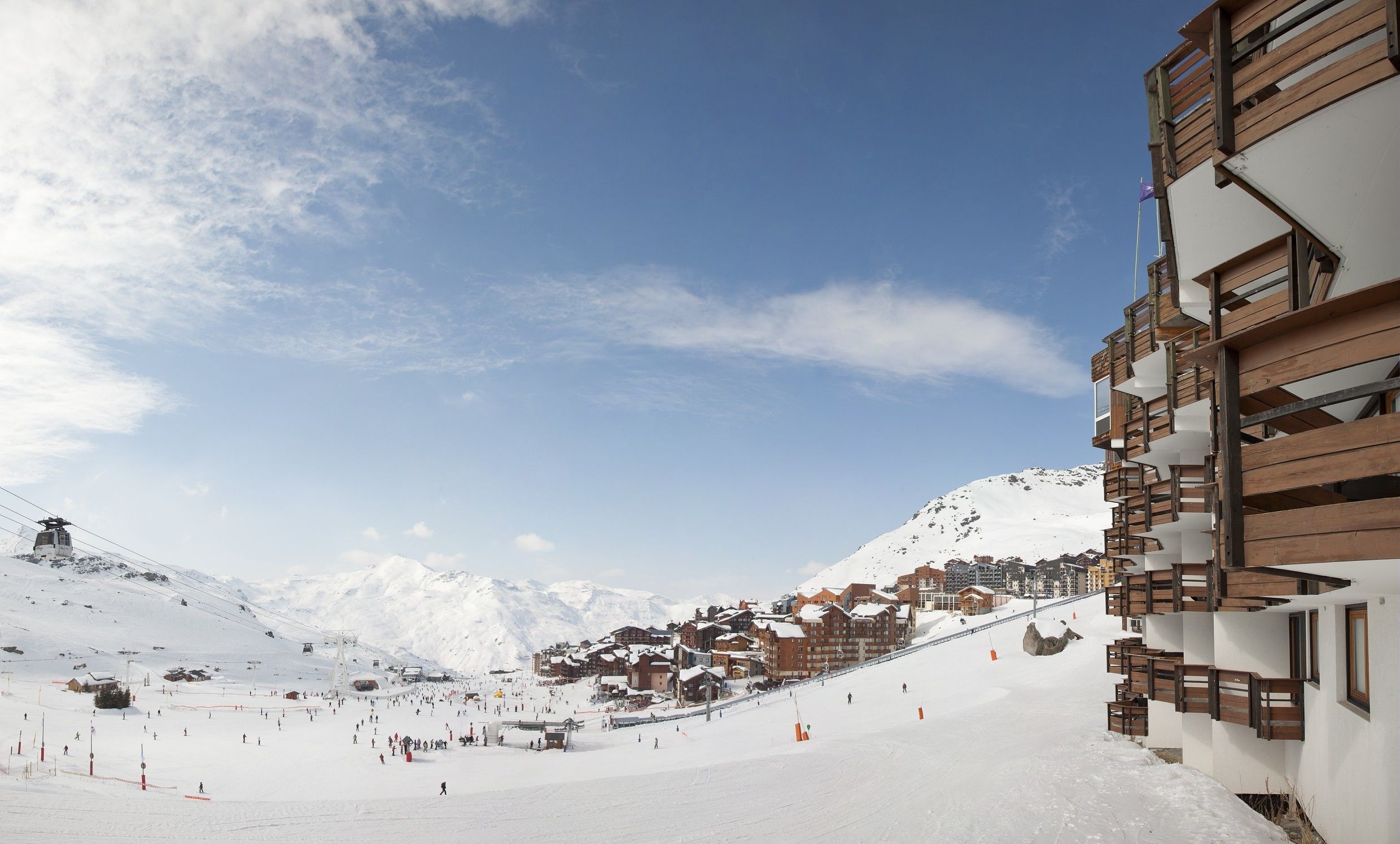 Estación de esquí nevada con telesilla, edificios y montañas al fondo.