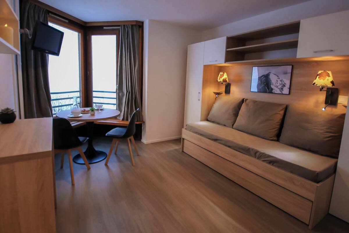 Ein modernes Zimmer mit Schreibtisch aus Holz, einer Couch und einem an der Wand befestigten Fernseher.