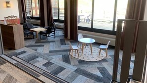 Un espace de détente intérieur doté d’un sol à motifs, d’une petite table avec des chaises et offrant une vue sur l’extérieur grâce à de grandes fenêtres.