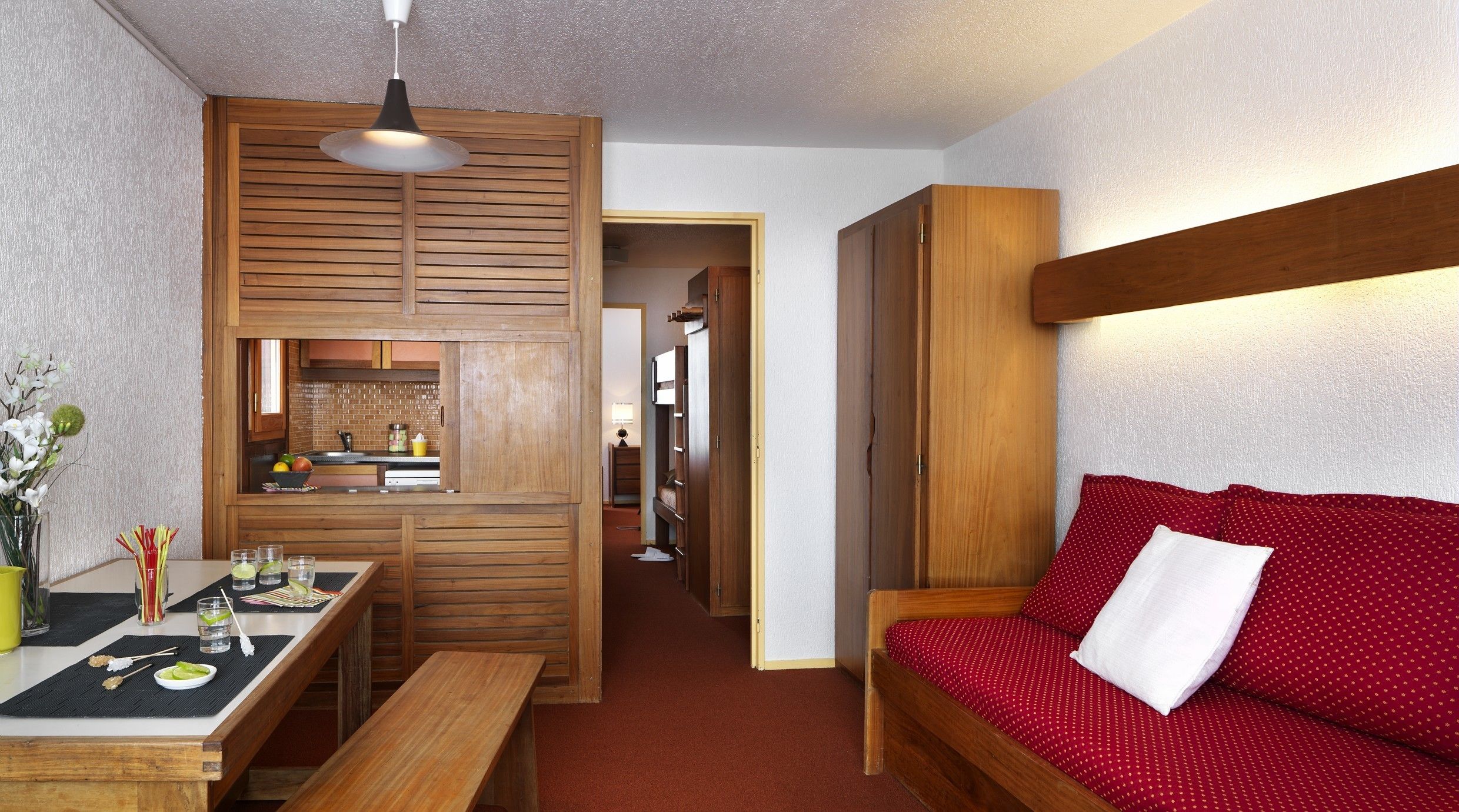 A compact room with a kitchenette, a dining area, and a bed with a red polka dot bedspread.