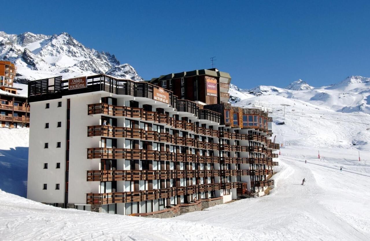 Un hotel de varios pisos con balcones, con una imponente montaña nevada de fondo.