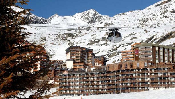 Une montagne enneigée, dotée d’un télésiège et d’un hôtel à plusieurs étages avec des balcons.