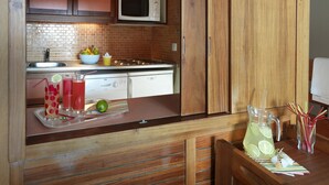 Une cuisine compacte équipée d’un four à micro-ondes, d’un évier et d’une cuisinière. On y trouve une petite table avec une carafe de limonade et un saladier rempli de fruits.