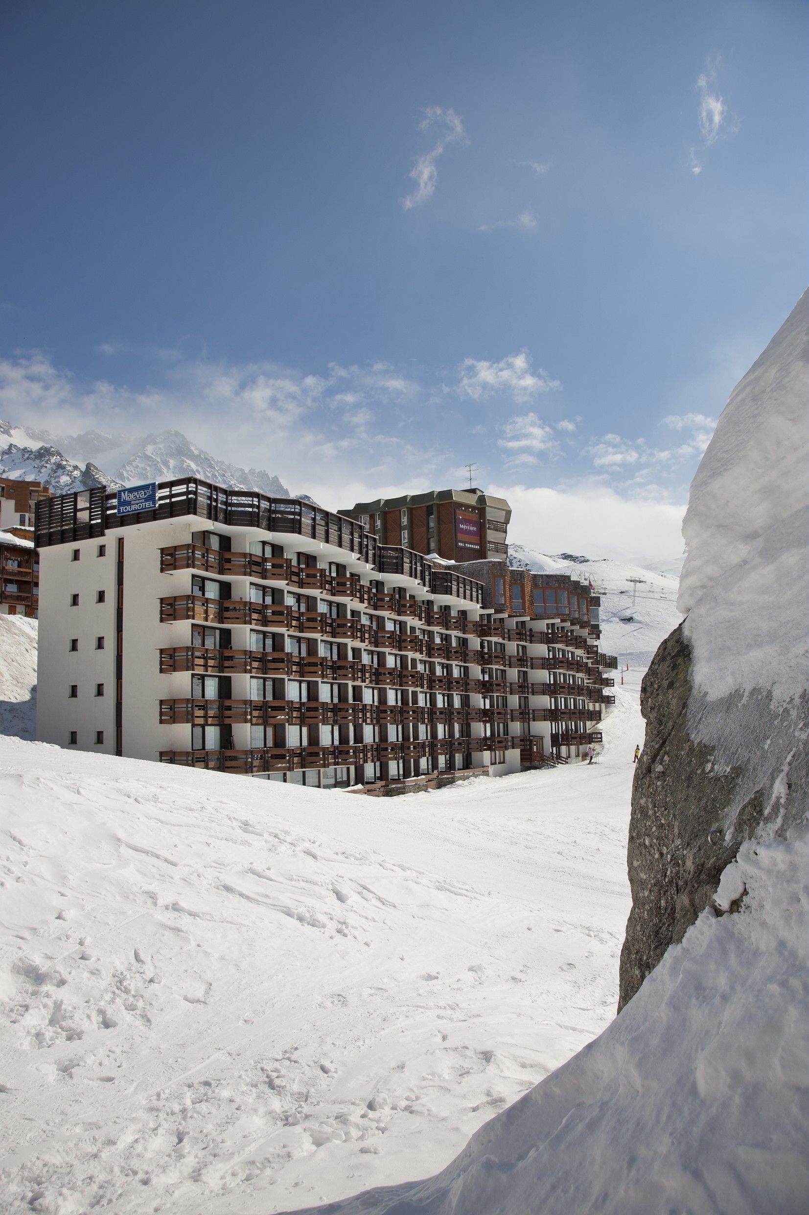 Et hotel med flere etager og balkoner, med et sneklædt bjerg i baggrunden.