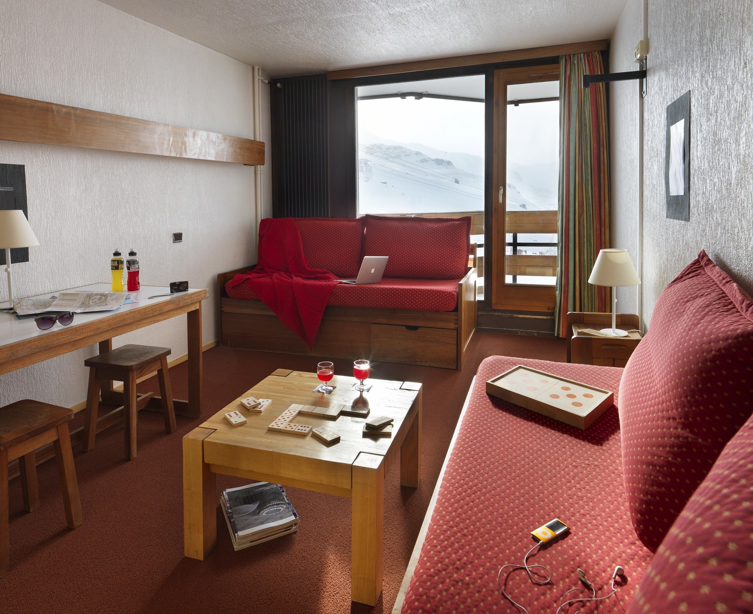 Een gezellige kamer met een houten bureau, een rode bank, een kleine tafel met gezelschapsspellen en een laptop op de bank.