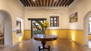 Una habitación con una mesa redonda de madera, un jarrón con flores amarillas y un cuadro en la pared.