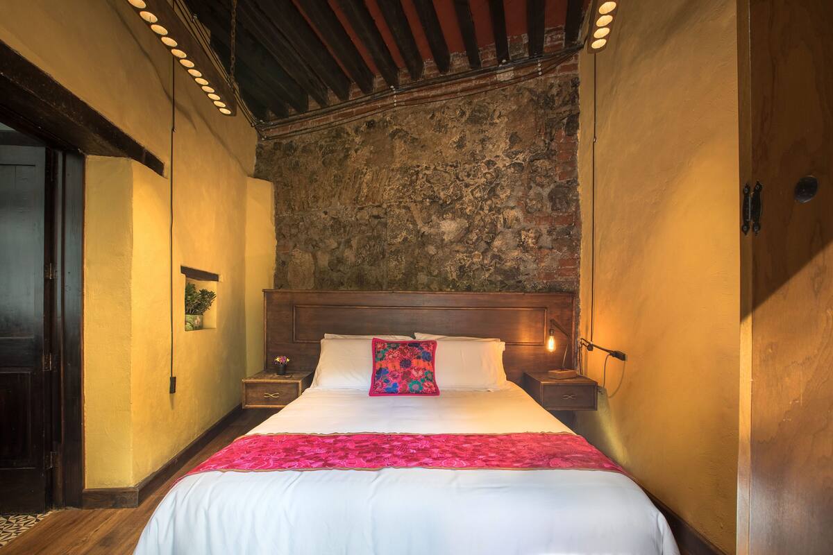 A hotel room with a large bed, wooden headboard, and a stone wall.
