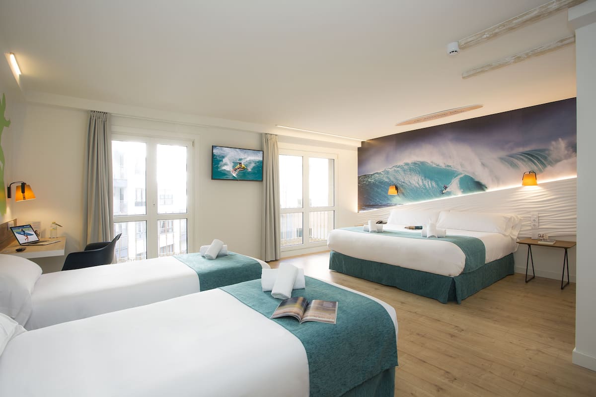 Une chambre d’hôtel avec deux lits, un bureau, une chaise, une télévision et une grande fresque murale sur le thème des vagues.
