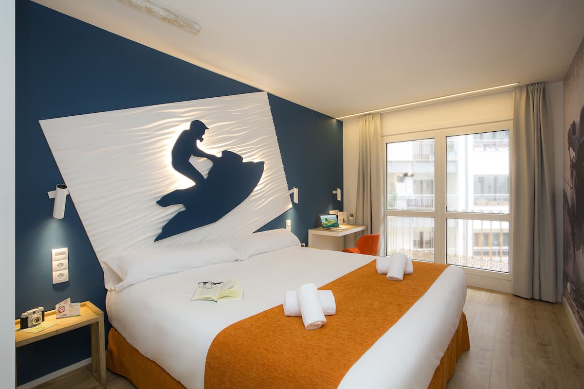 Une chambre d’hôtel avec un lit, une table de chevet, une fenêtre donnant sur un paysage agréable et un tableau au mur.