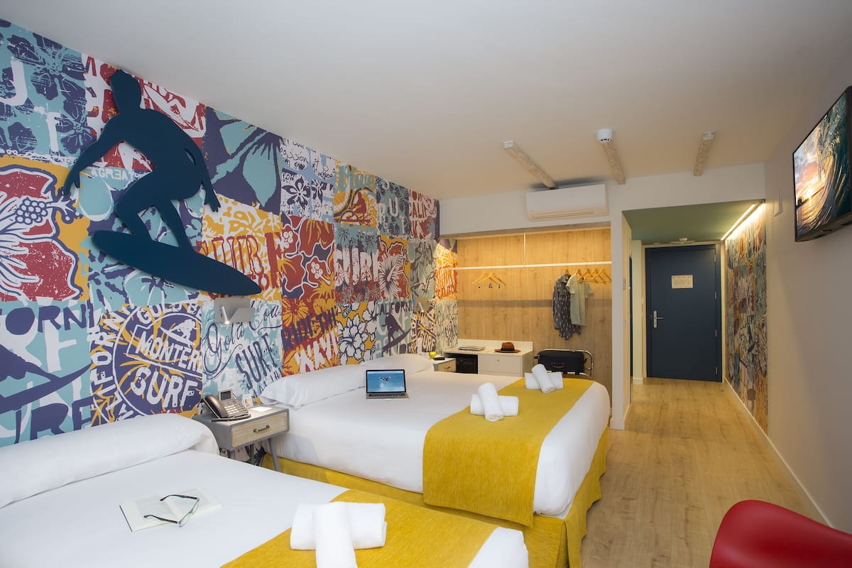 Une chambre d’hôtel avec deux lits, un ordinateur portable posé sur l’un des lits et une fresque colorée sur le mur.