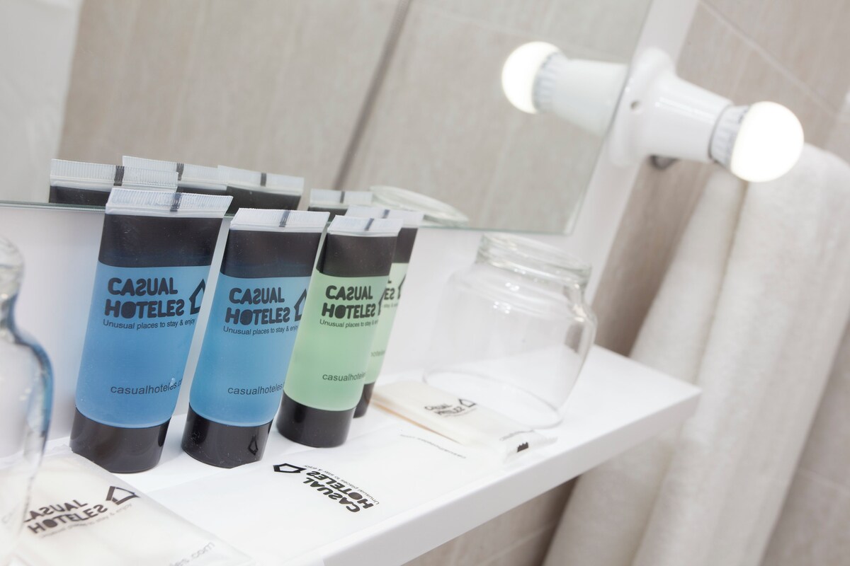 En badeværelseshylde med flere tuber 'Casual Hotel' produkter, en glasbeholder og et hvidt håndklæde.