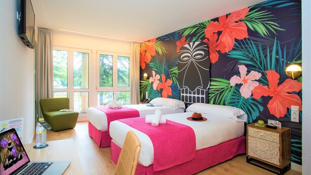 Ein Hotelzimmer mit zwei Betten, einem Laptop, einem Sessel, einem Nachttisch und einem großen floralen Wandbild.