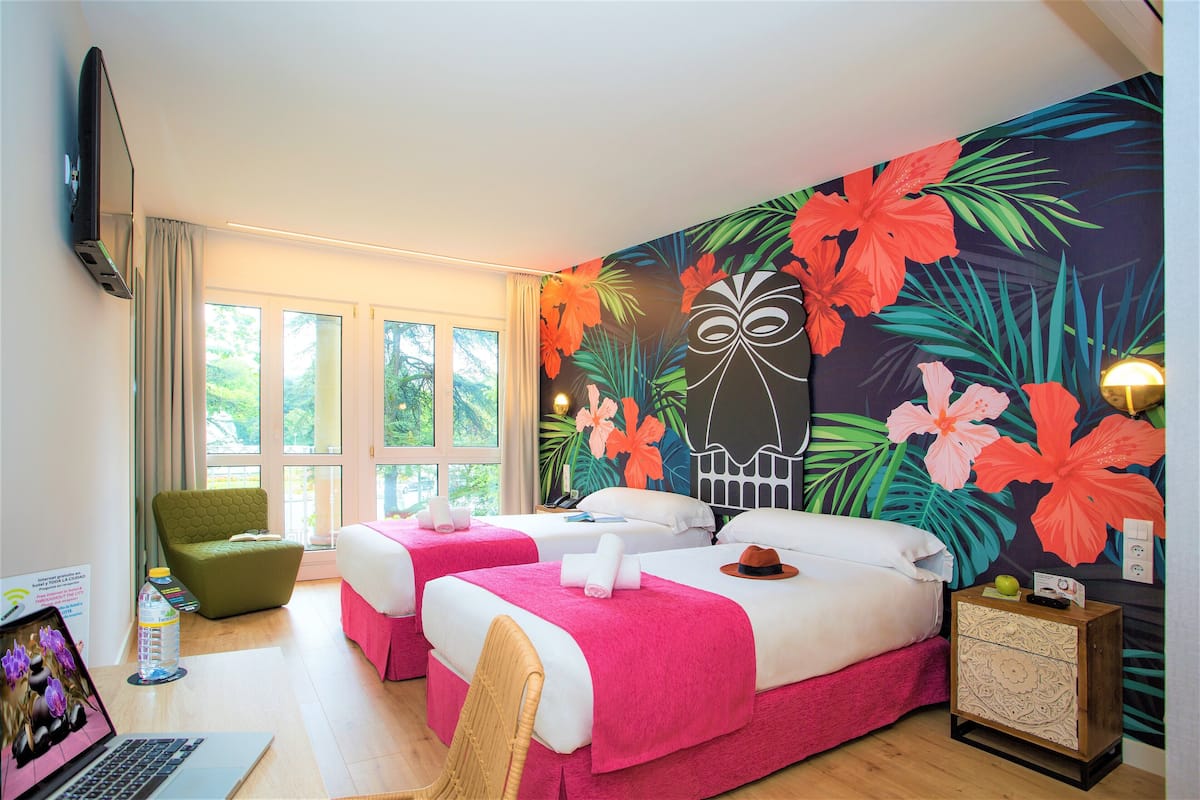 Une chambre d’hôtel avec deux lits, un ordinateur portable, une chaise, une table de chevet et une grande fresque florale sur le mur.