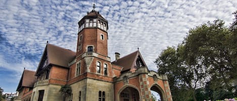A historic building with a prominent tower, arched windows, and a well-maintained garden.