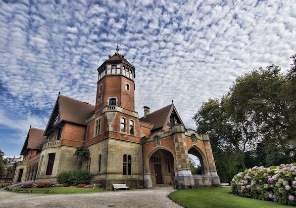 A historic building with a prominent tower, arched windows, and a well-maintained garden.