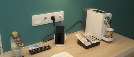 A desk with a laptop, smartphone, remote, book, glasses, water bottle, and a coffee machine.