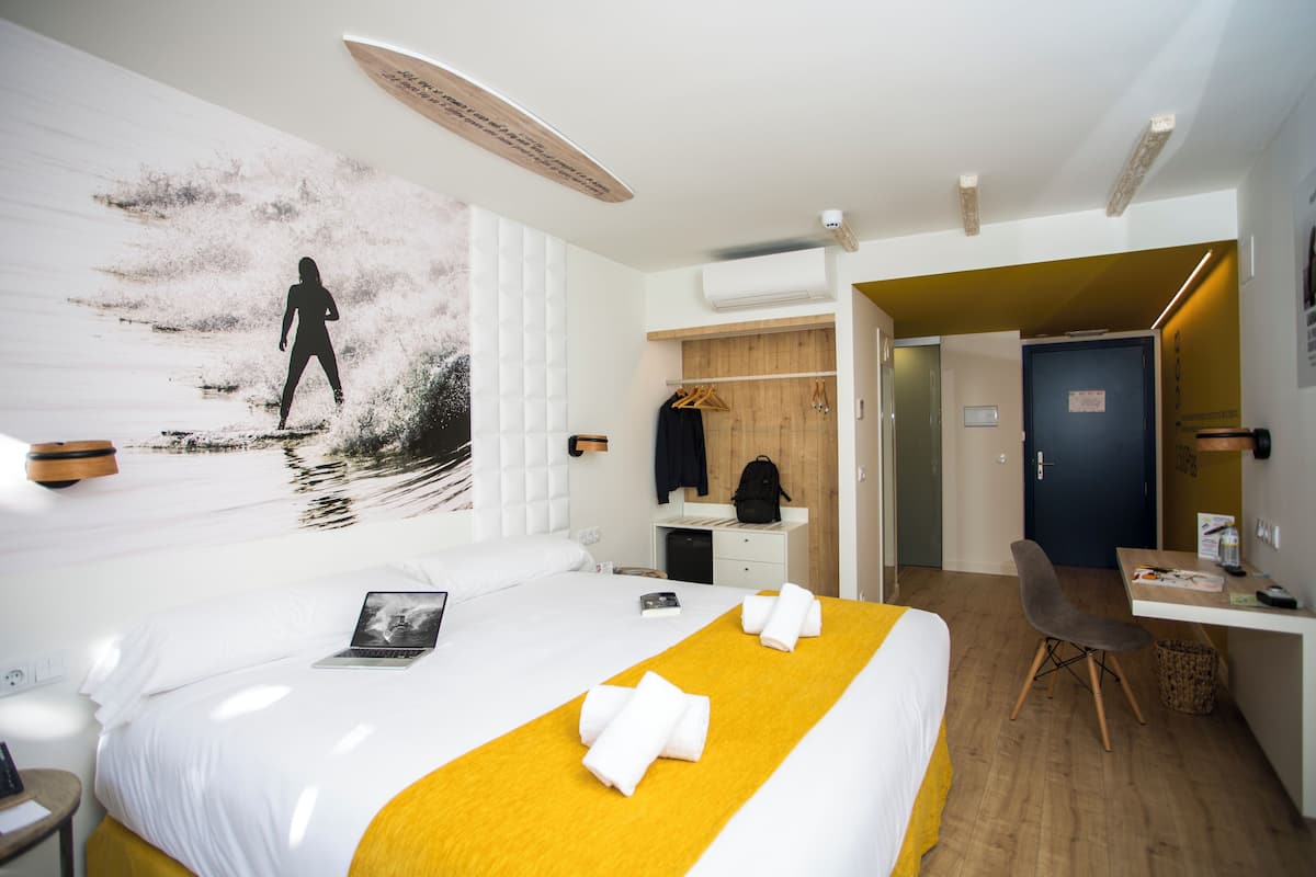 Une chambre d’hôtel comprenant un lit, un bureau, une chaise, une étagère fixée au mur et une porte.