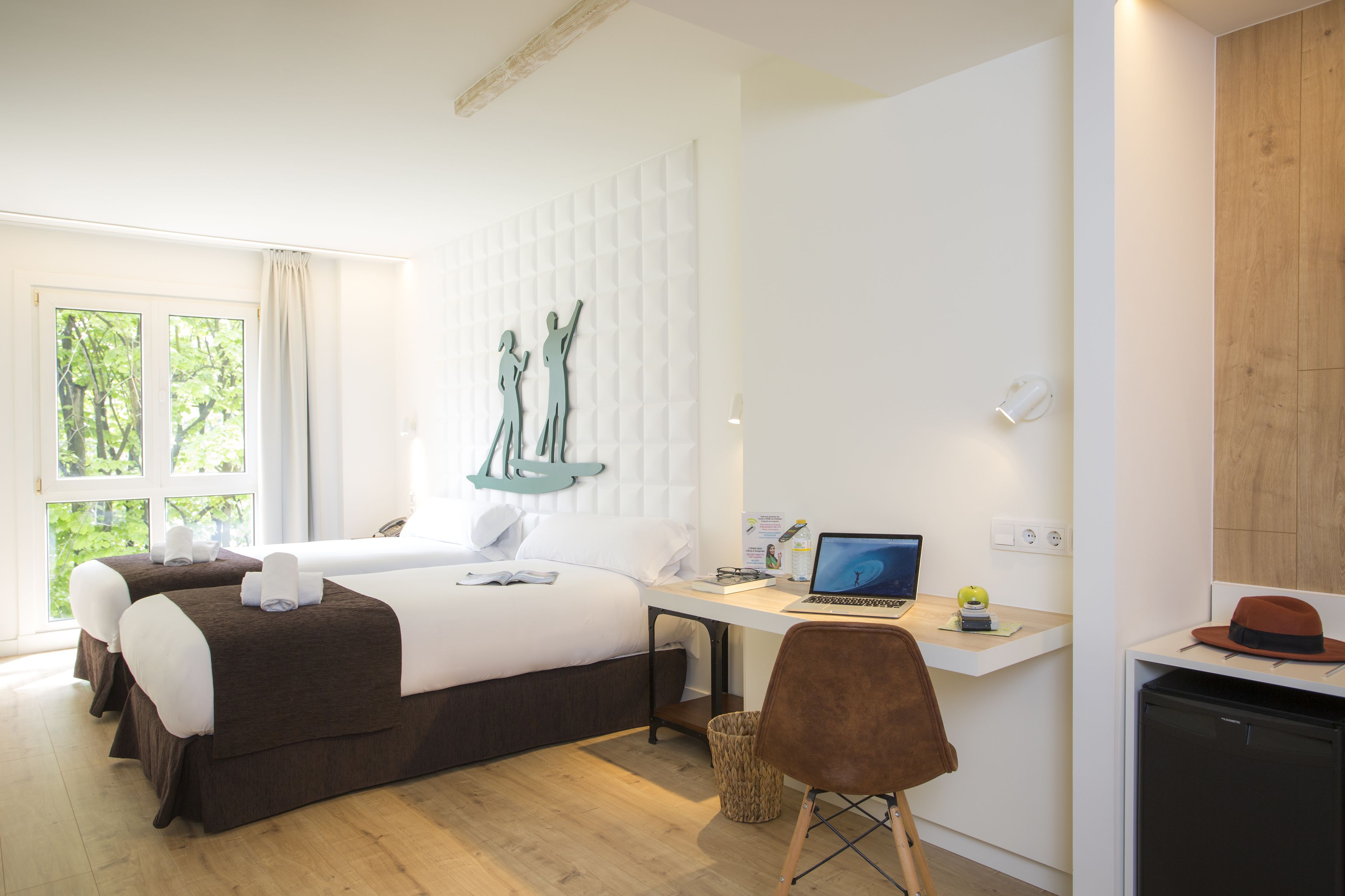 Une chambre d’hôtel avec un lit, un bureau, un ordinateur portable et une vue sur la verdure environnante.