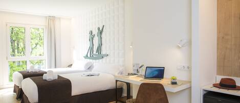 Une chambre d’hôtel avec un lit, un bureau, un ordinateur portable et une vue sur la verdure environnante.