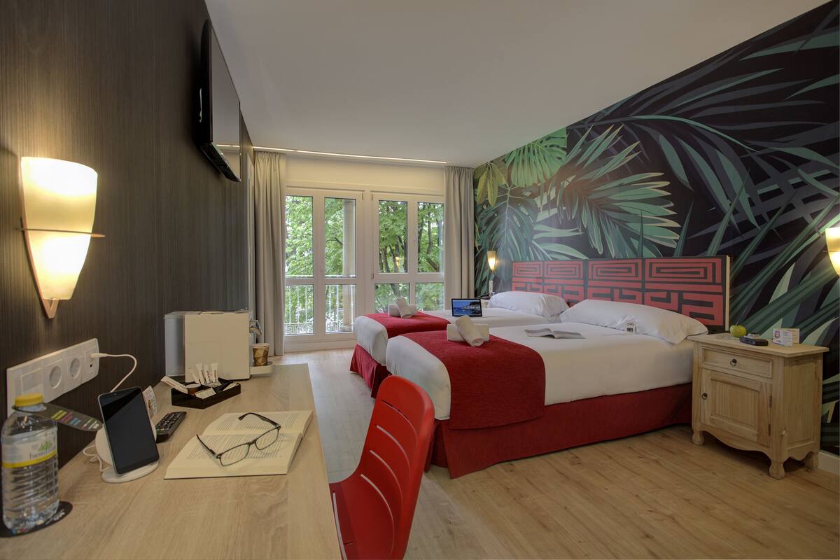 Une chambre d’hôtel avec deux lits, un bureau avec un ordinateur, une chaise, une table de chevet et une grande fenêtre.