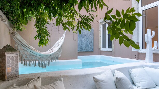 A poolside area with a hammock, a cactus sculpture, and a white sofa with cushions. - Garam Lisboa (Lisbon)