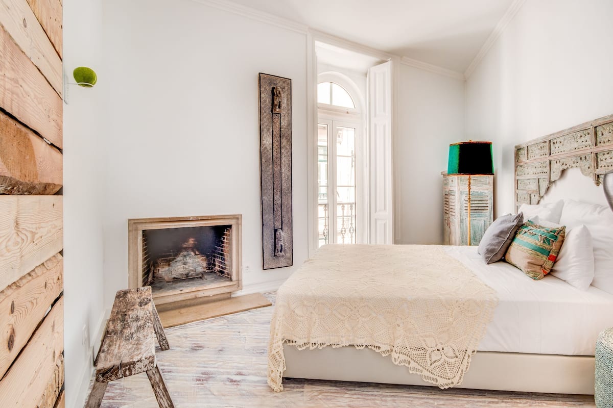 A bedroom with a bed, a fireplace, a wooden wall, and a window.