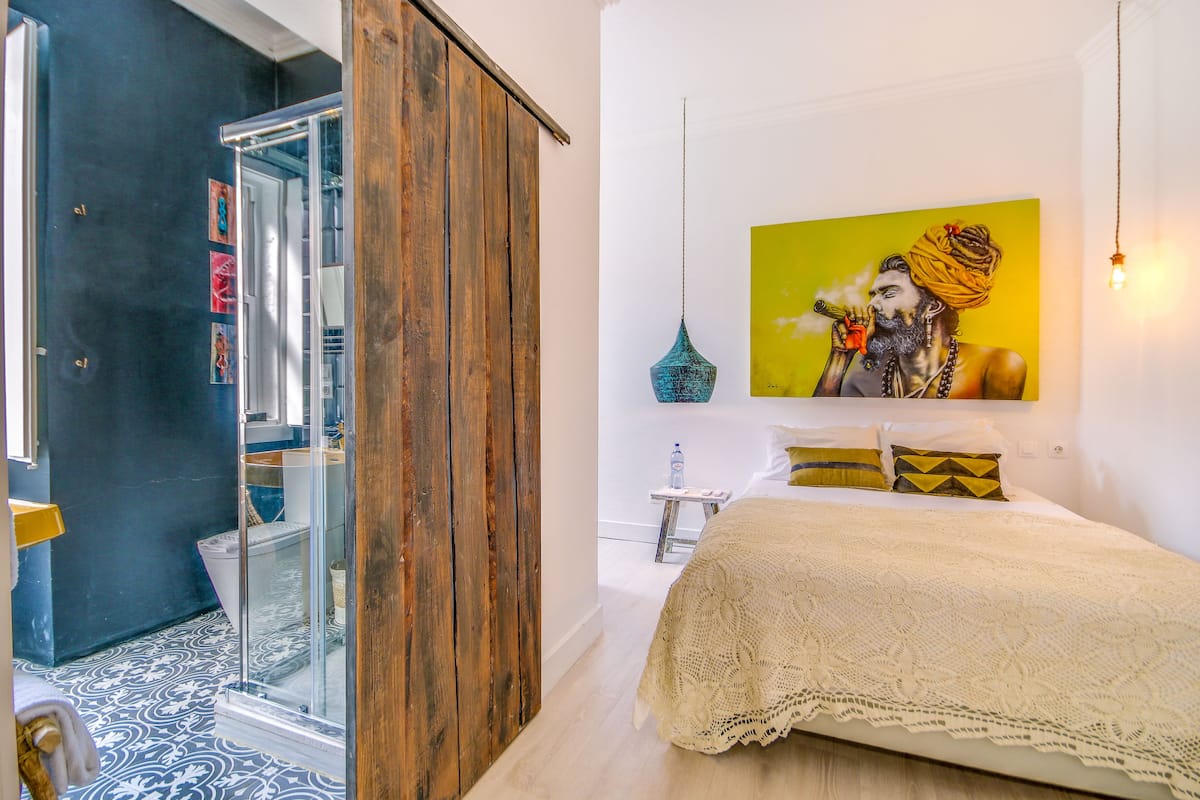 A bedroom with a large bed, a glass shower, and a painting on the wall.
