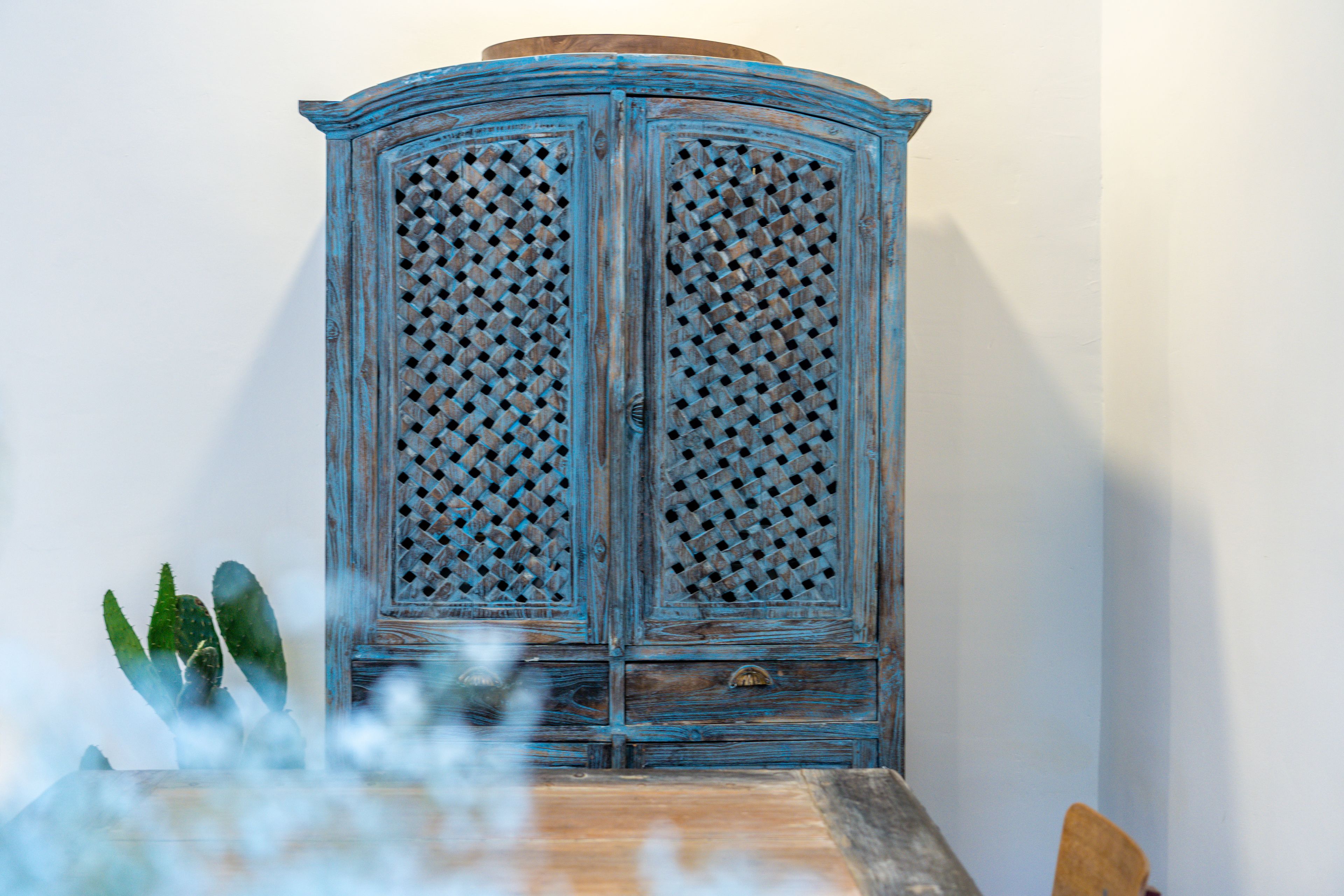 A blue wooden cabinet with a lattice design, placed against a white wall.
