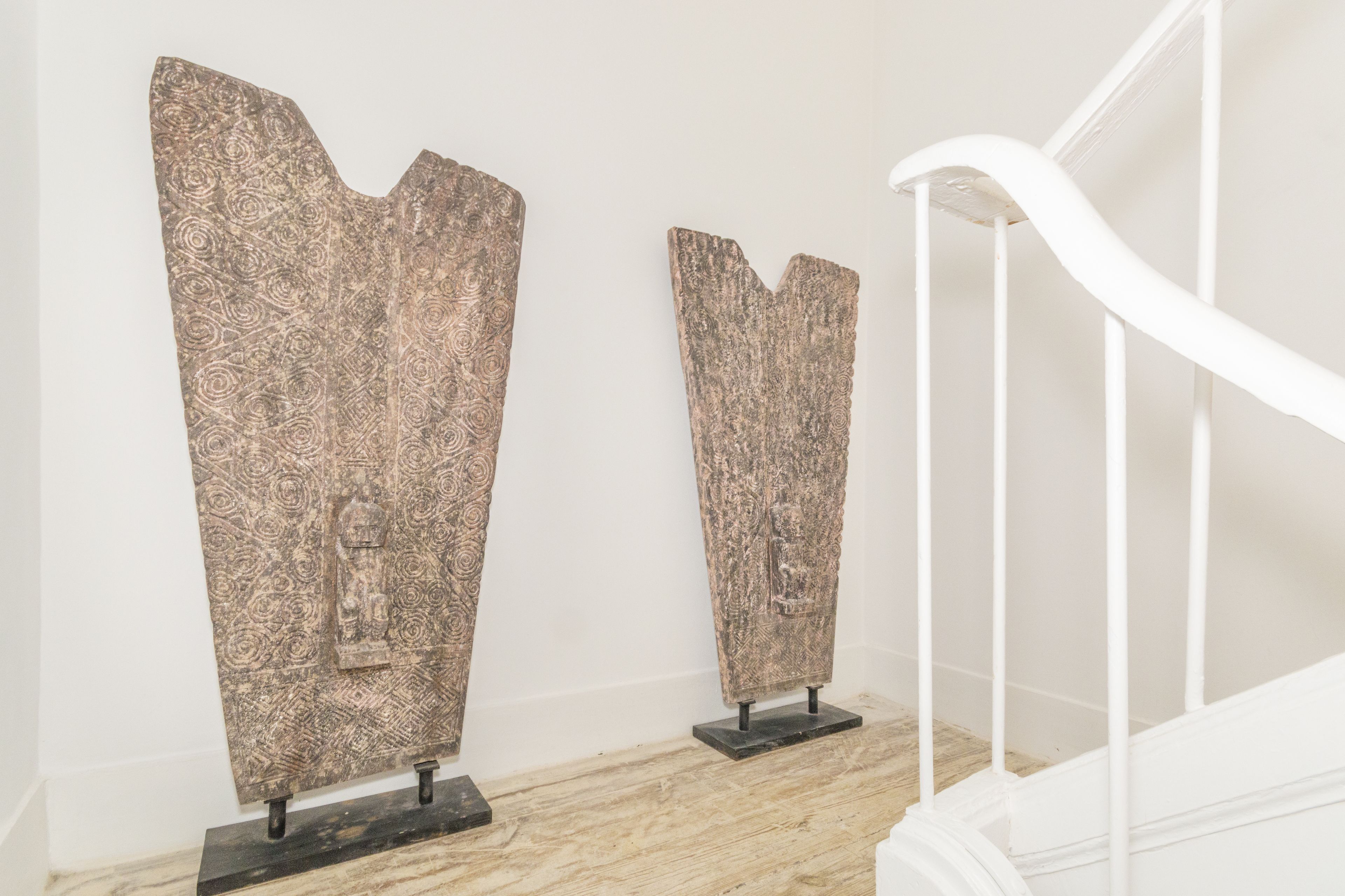 Two abstract sculptures on black pedestals against a white wall, with a white staircase in the background.