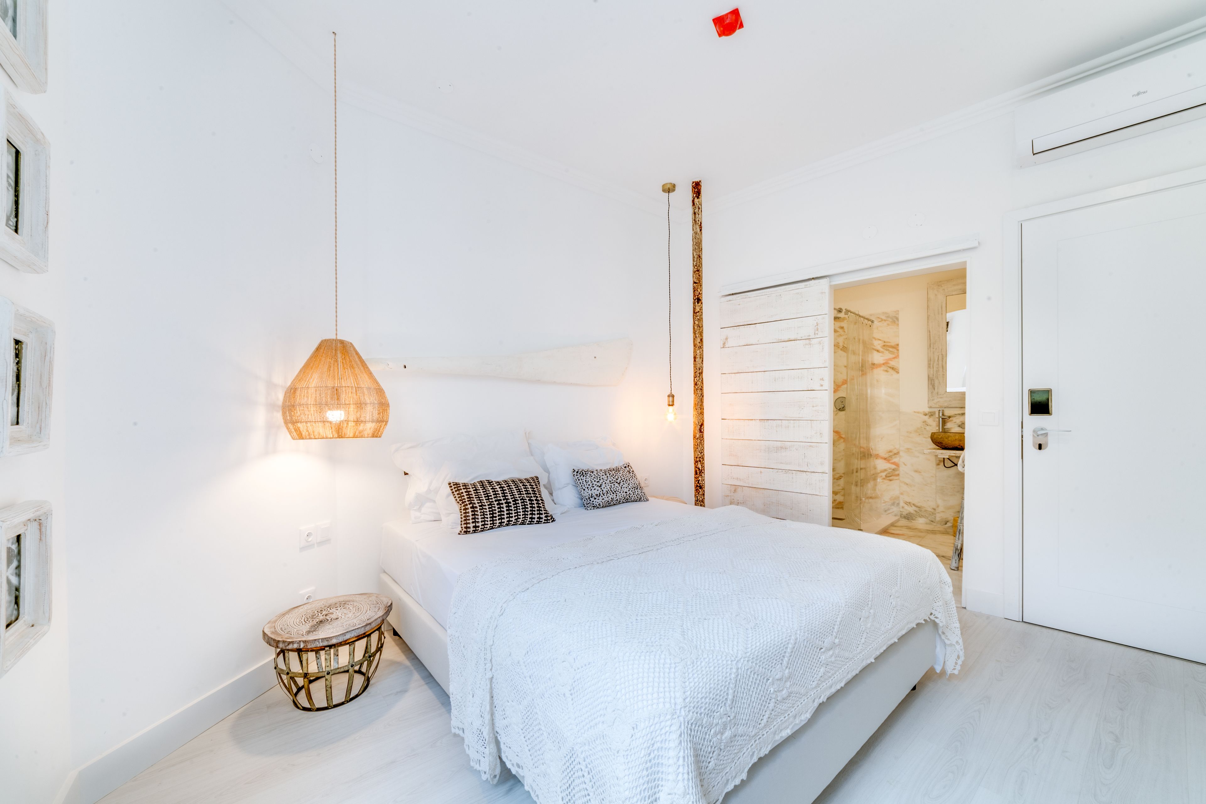 Um quarto com uma cama grande, uma luminária de cabeceira, uma mesinha redonda e uma porta que dá para um banheiro.