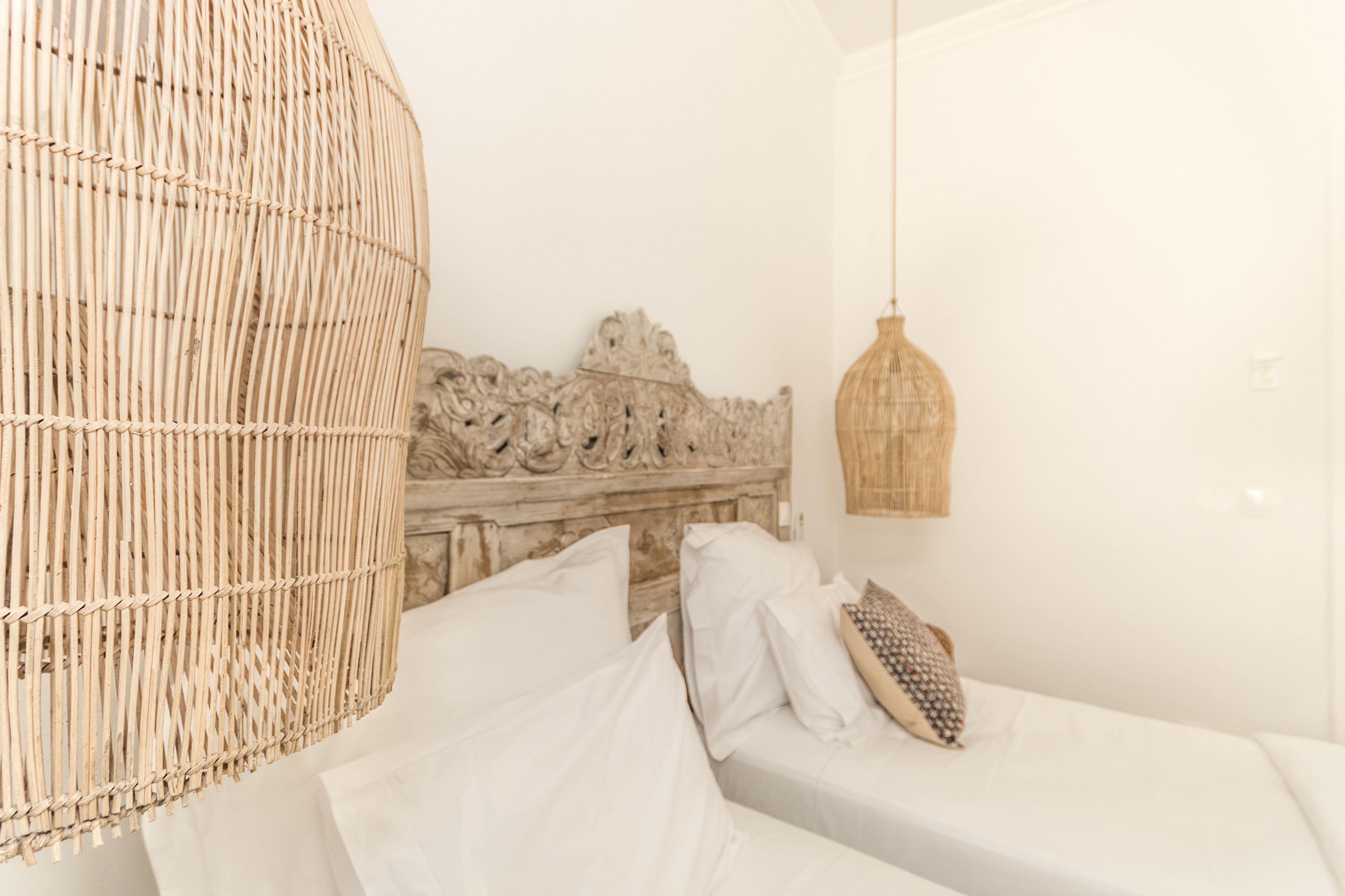 A room with a bed, a woven hanging chair, a carved headboard, and a hanging light fixture.