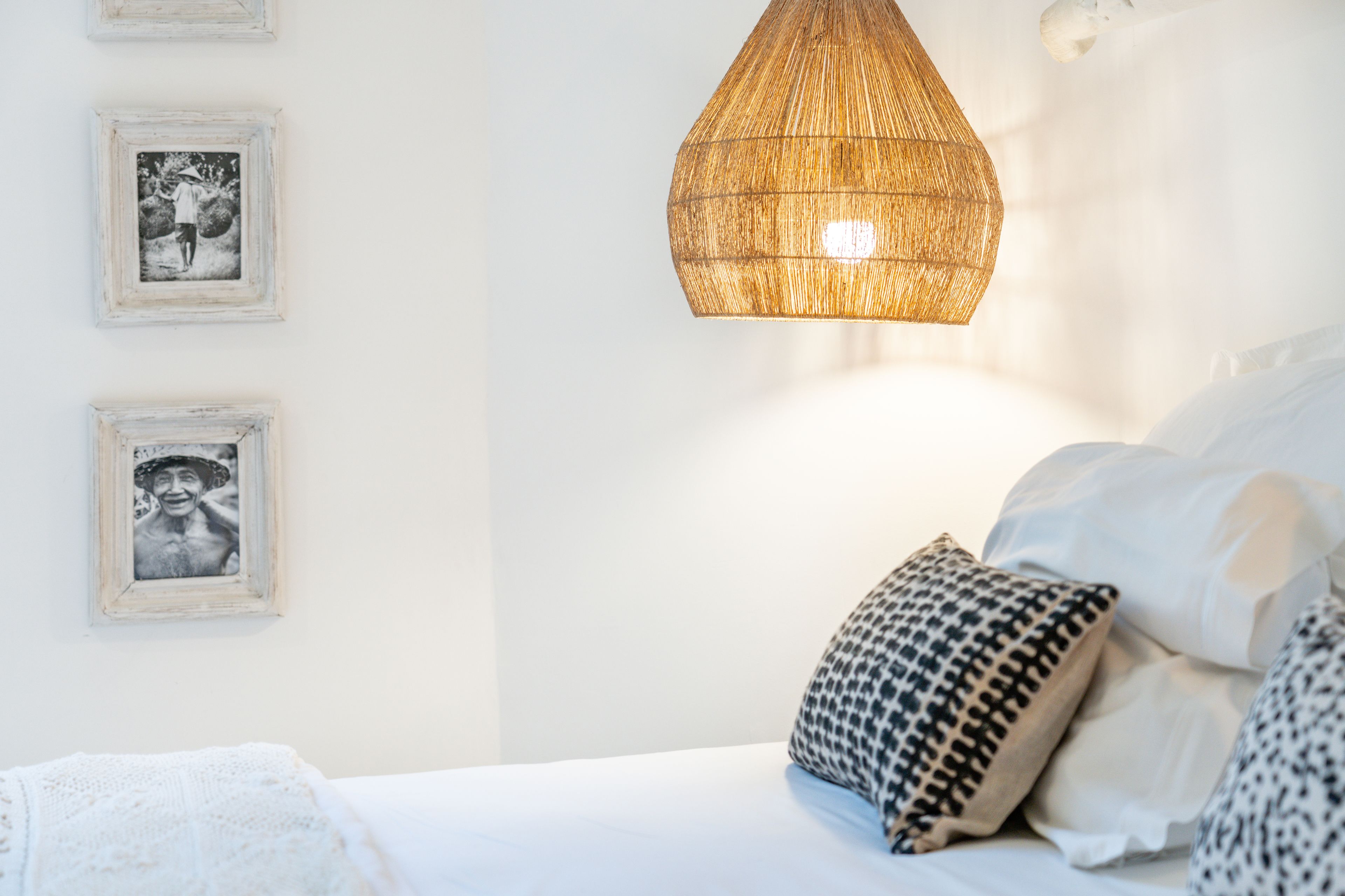A bedroom with a bed, white bedding, a patterned pillow, and a hanging light fixture.