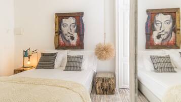 A bedroom with a bed, pillows, a bedside lamp, a small wooden stool, and a mirror.