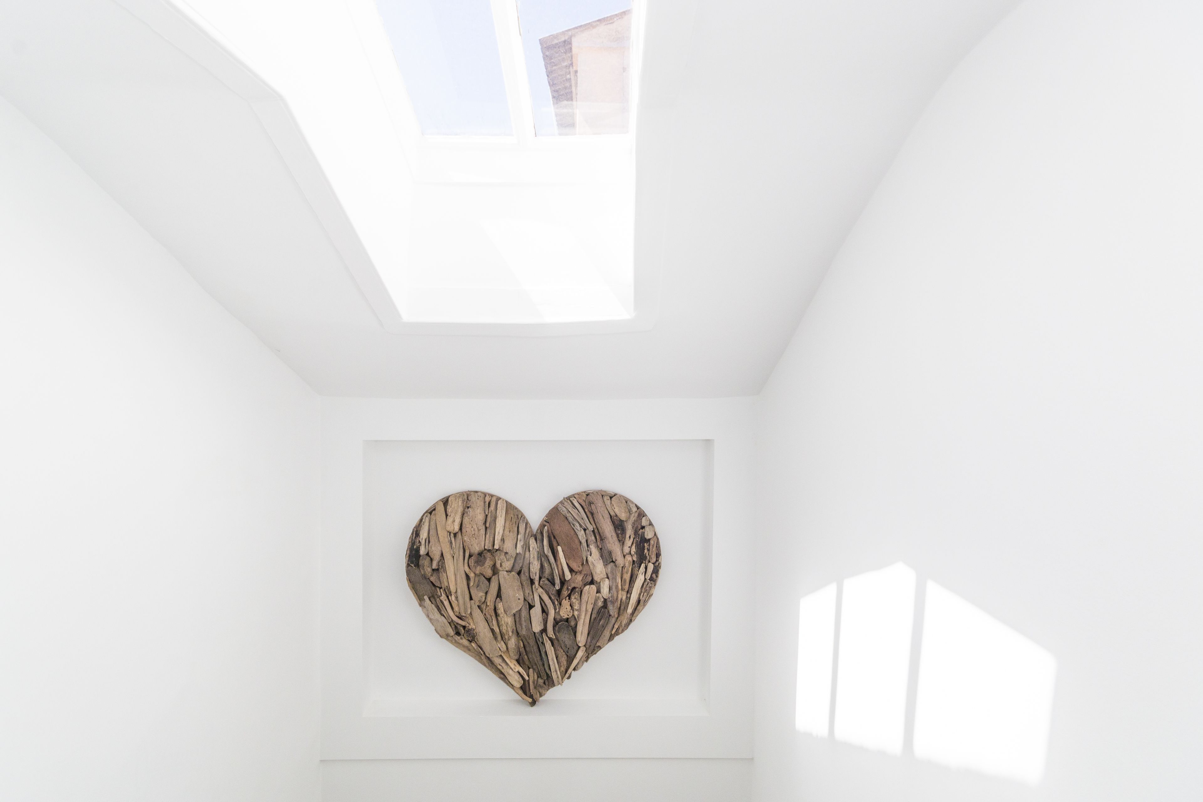 Una habitación con tragaluces, una obra de arte de madera con forma de corazón y una pared blanca.