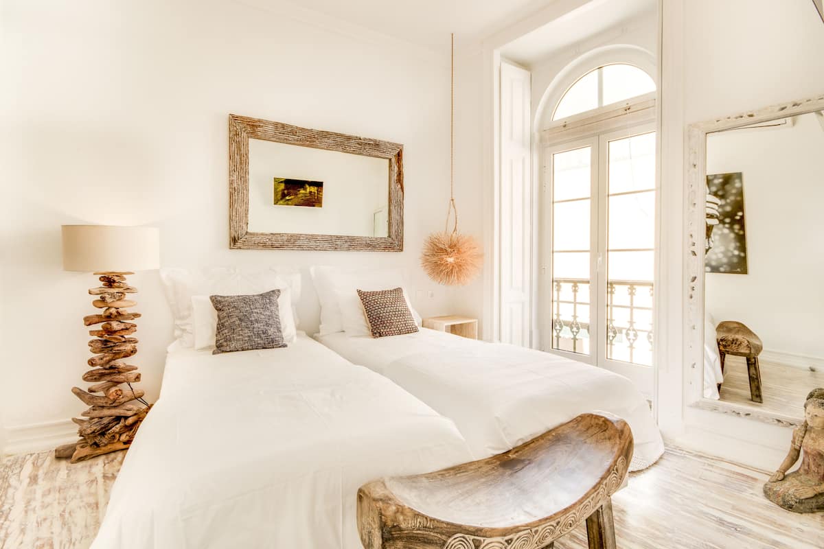 A bedroom with a large bed, a wooden bench, a mirror, and a hanging light fixture.