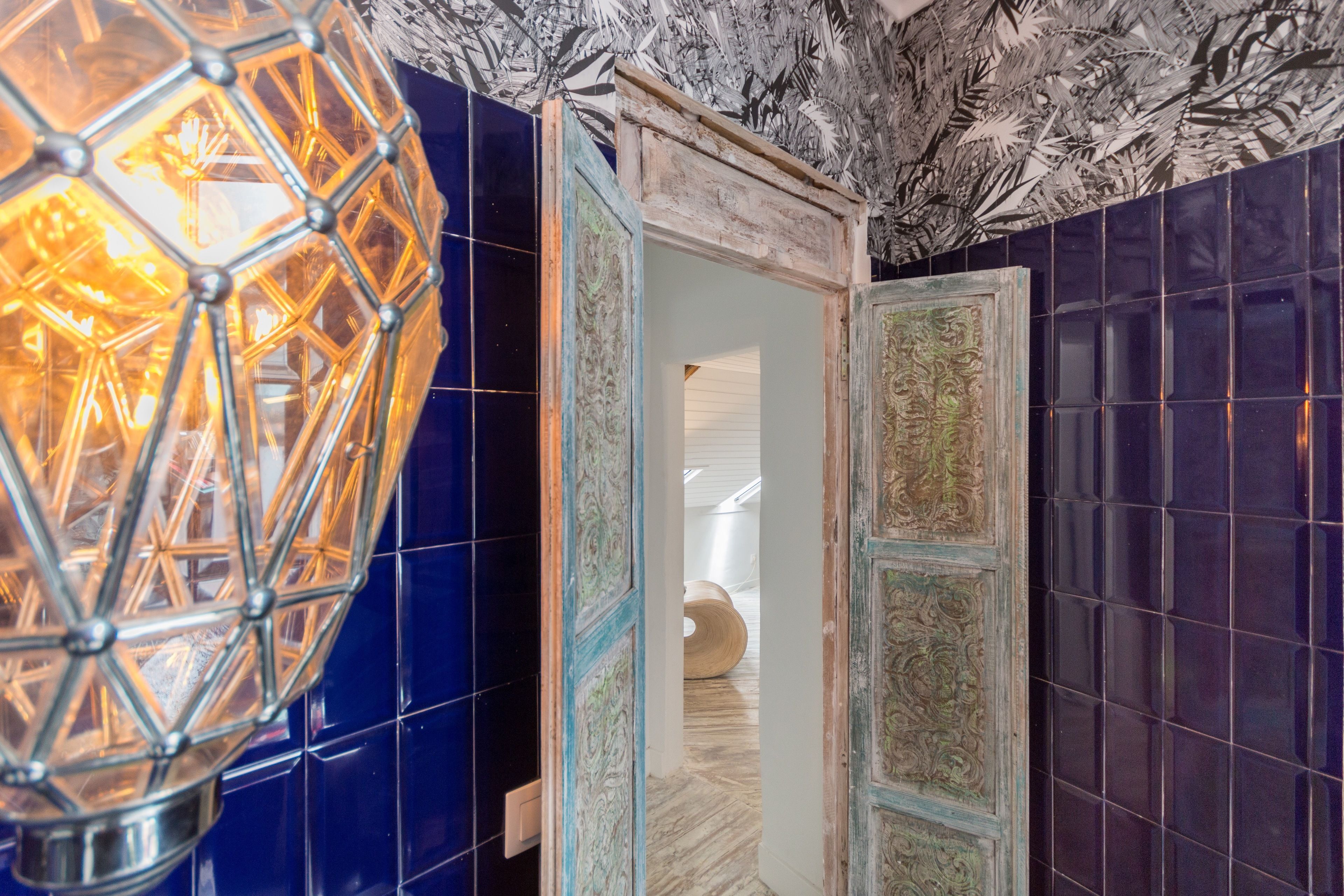 A room with a geometric light fixture, a wooden door with intricate designs, and a patterned ceiling.