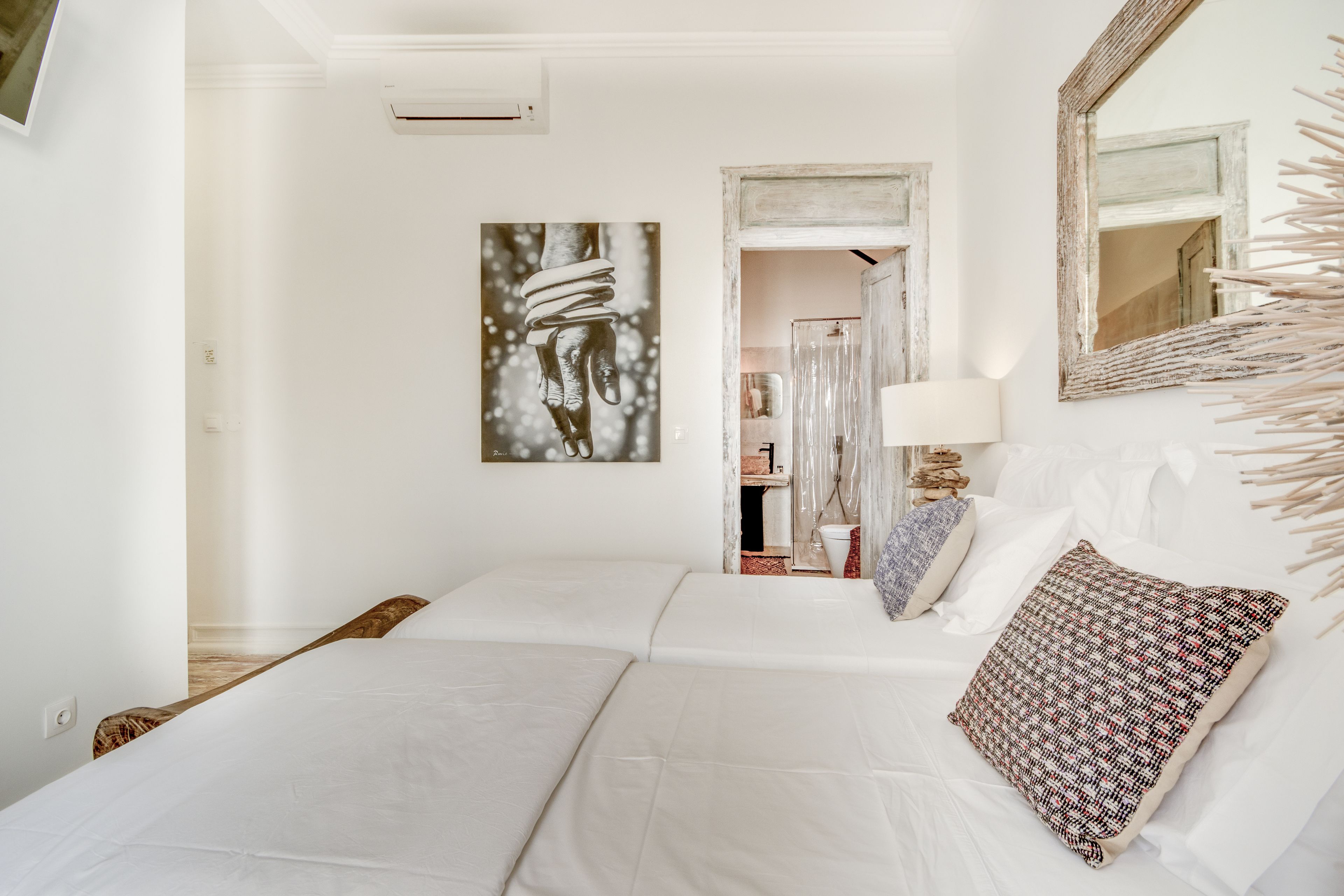 Una habitación de hotel con dos camas, un espejo grande, una obra de arte colgada en la pared y un baño visible a través de una puerta abierta.