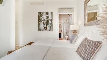 Una habitación de hotel con dos camas, un espejo grande, una obra de arte colgada en la pared y un baño visible a través de una puerta abierta.