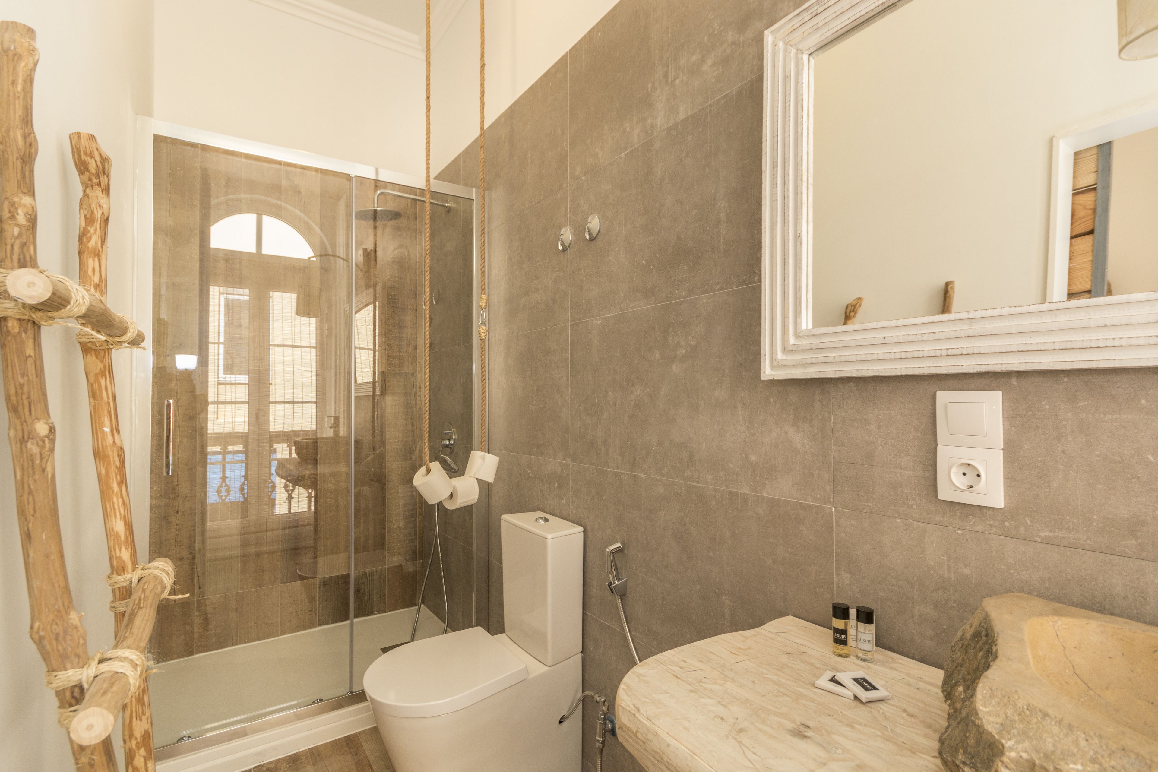A bathroom with a glass shower enclosure, a toilet, a sink with a stone countertop, and a mirror above the sink.