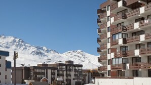 Un hotel de varios pisos con balcones, un centro de esquí al fondo y montañas cubiertas de nieve.