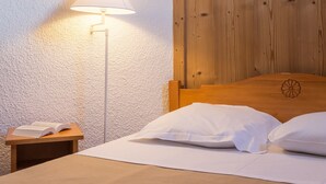 Un dormitorio con cabecera de madera, una mesita de noche con un libro abierto y una lámpara de pie.