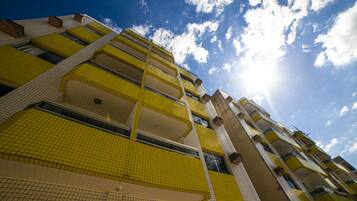 Edifício de vários andares com varandas azulejadas em amarelo e céu claro.