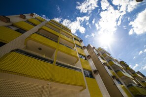 Edifício de vários andares com varandas azulejadas em amarelo e céu claro.