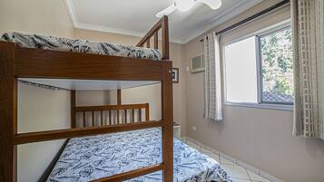 Uma cama beliche com edredom estampado, uma janela com cortinas e um lustre no teto.