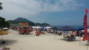 A beach with food stalls, umbrellas, and beach chairs. - Apto 22E ar condicionado e ventilador, 2 quartos, churrasqueira, elevador e piscina (Ubatuba)