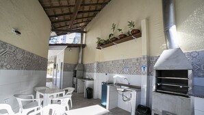 A compact kitchen with a built-in oven, a sink, and a small dining area with chairs. - Apto 22E ar condicionado e ventilador, 2 quartos, churrasqueira, elevador e piscina (Ubatuba)