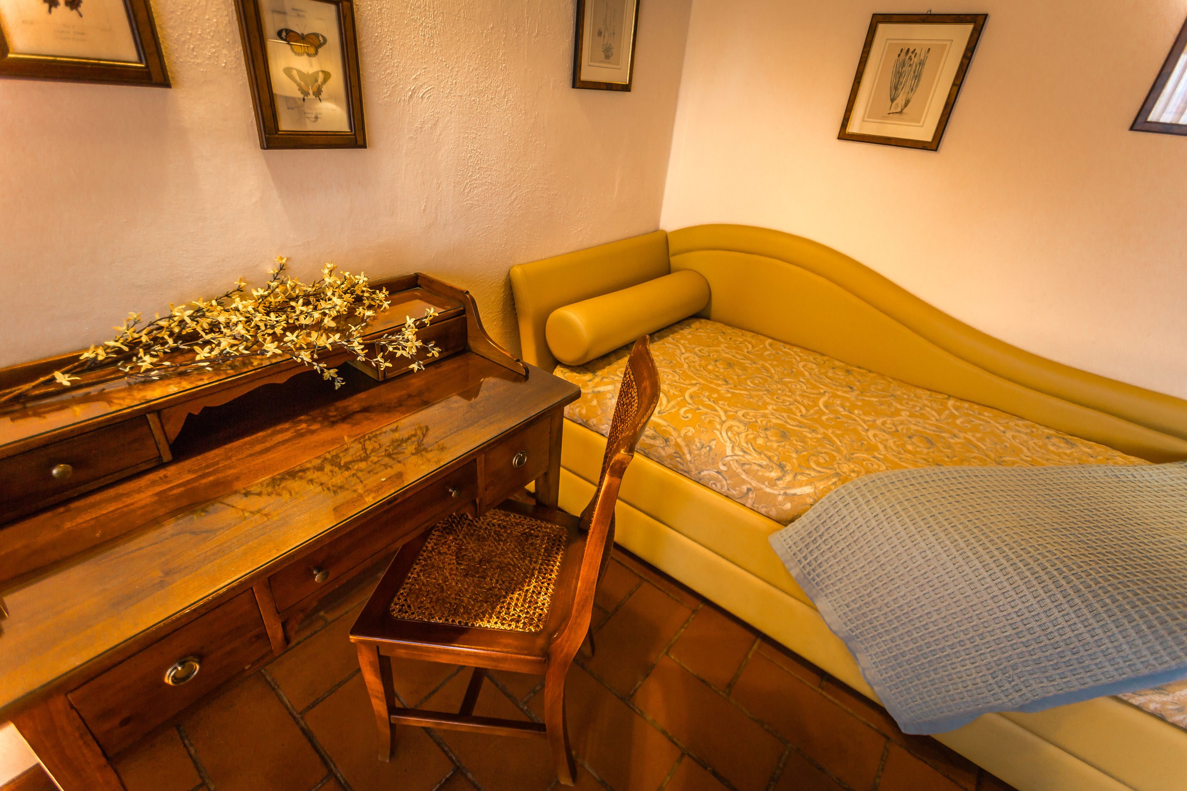 A compact bedroom with a wooden desk, a yellow sofa bed, and a patterned bedspread.