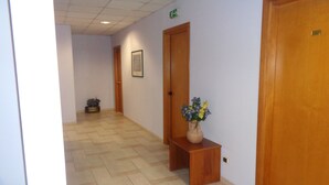 A hallway with a wooden bench, a vase of flowers, and a door with an exit sign. - Hotel Millennium (Orte)