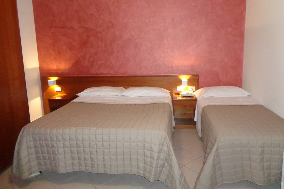 A hotel room with two single beds, each with a wooden headboard and bedside lamps.