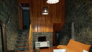 Ein gemütliches Interieur mit Kamin aus Stein, einer Holztreppe und einem Essbereich mit Tisch und Stühlen.